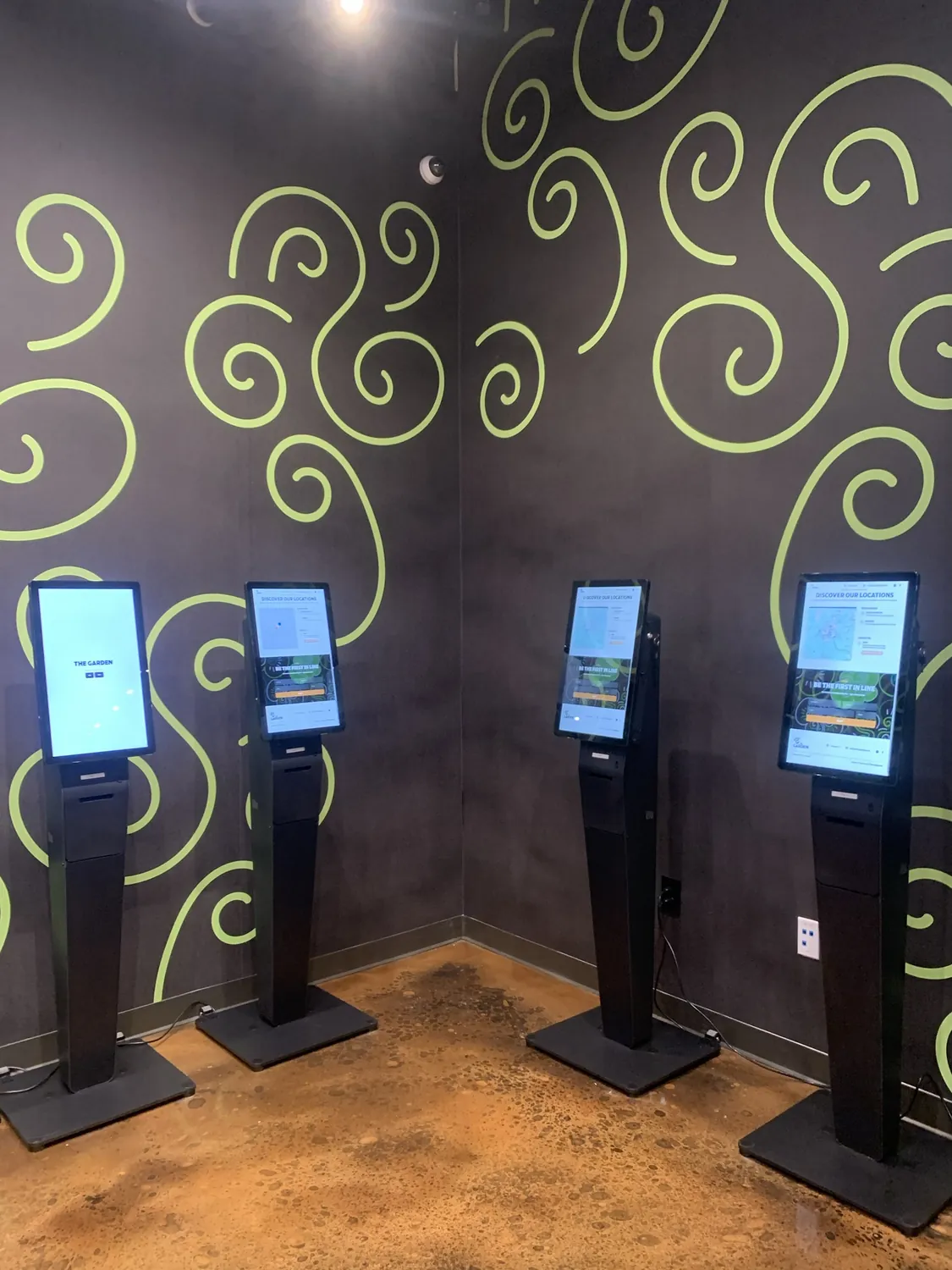 Self-service ordering kiosks lined up along the wall inside The Garden